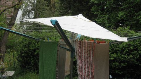 Ein Wäschespinner steht im Garten und ist mit einem Schirm vor Regen geschützt, während Wäsche zum Trocknen hängt.