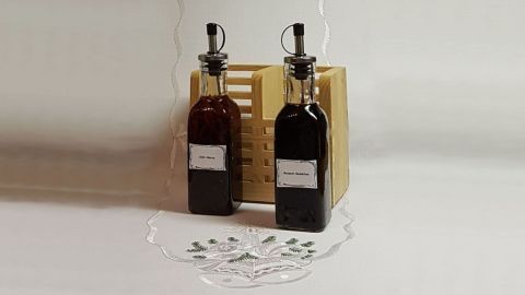 Zwei Flaschen mit Chili-Sherry-Reduktion stehen auf einem Holzständer, umgeben von einer minimalen, hellen Kulisse.