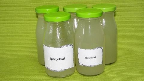 Fünf Gläser Spargelsud stehen auf einem grünen Hintergrund, bereit zur Verwendung in einer Gemüsezubereitung.