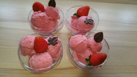Weiche Erdbeereisportionen in Schalen, dekoriert mit frischen Erdbeeren, auf einer Holzunterlage präsentiert.
