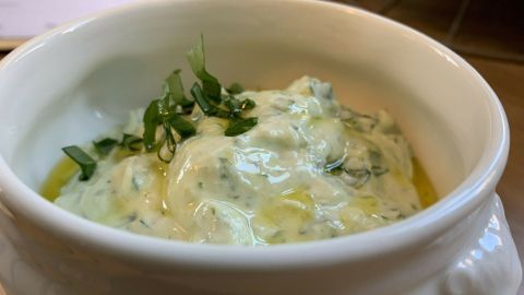 Eine Schüssel mit feinem Bärlauchquark, cremig und garniert mit frischen Kräutern, steht auf einer hellen Oberfläche.