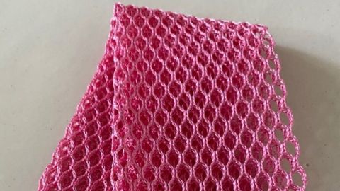 Ein pinkfarbener Geschirrwäsche-Netztuch liegt auf einer hellen Oberfläche und wartet darauf, zum Reinigen von Arbeitsflächen verwendet zu werden.