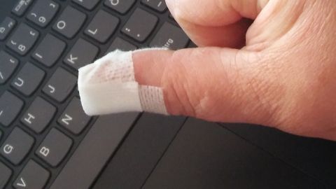 Ein weißer Pflasterverband bedeckt die verletzte Fingerkuppe einer Hand, die auf einer Laptop-Tastatur ruht.