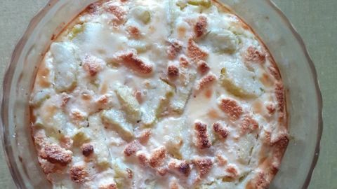 Ein golden-braunes Gratin aus Rhabarber und Zwieback wird in einer durchsichtigen Glasform serviert, auf einem Holzuntergrund.