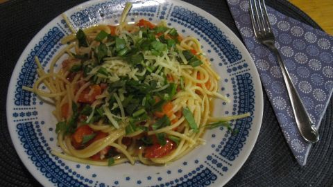 Ein Teller Spaghetti mit Schinken und Gemüse wird garnierte mit frischen Kräutern, serviert auf einem dekorativen Teller.