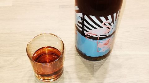 Eine Flasche Amaretto steht neben einem Glas mit einem dunklen, aromatischen Getränk auf einem Holzuntergrund.