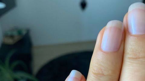 Gesunde, gepflegte Nägel zeigen eine Hand, die in einem hellen Raum mit Pflanzen im Hintergrund gehalten wird.