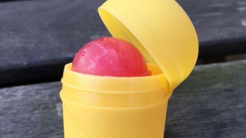 Eine gelbe Ü-Ei-Verpackung, die geöffnet ist und einen roten Lolli zeigt, steht auf einem Holztisch im Freien.