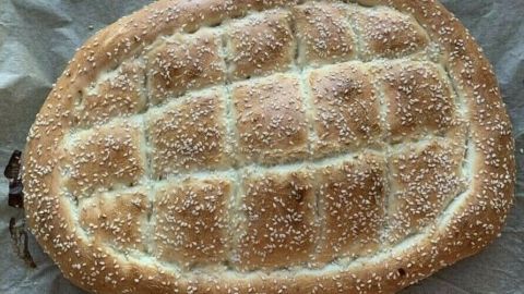 Ein frisch gebackenes türkisches Fladenbrot mit Sesam liegt auf einem Backblech, umgeben von Backpapier.