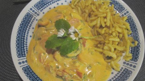 Leckeres Kurkuma-Schmand-Gemüse mit gebratenen Spätzle auf einem schön dekorierten Teller, umgeben von einem dunklen Tisch.