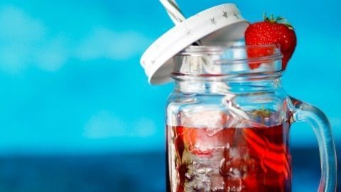 Ein Glas Erdbeerlimes steht auf einem Tisch, gefüllt mit rotem Getränk und Eis, umgeben von frischen Erdbeeren.
