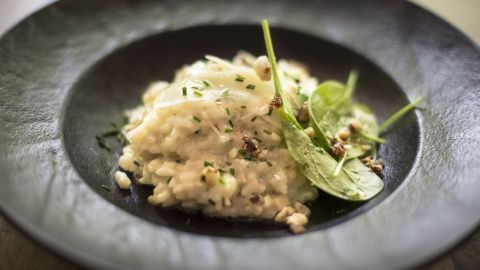 Ein cremiges Risotto ohne Käse wird in einer eleganten schwarzen Schale serviert und mit frischen Kräutern garniert.