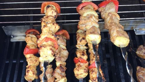 Saftige Schaschlik-Spieße werden auf einem Grill zubereitet, umgeben von rauchigem Ambiente und Grillgeräten.