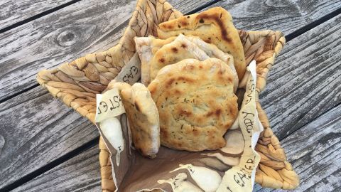 In einer dekorativen Schale liegen frisch gebratene Rosmarin-Pizzabrote auf einer rustikalen Holzoberfläche.