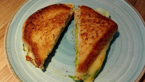 Ein knuspriges Sandwich liegt auf einem blauen Teller, halbiert, mit goldbrauner Kruste und geschmolzenem Käse sichtbar.