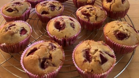 Saftige Erdbeer-Muffins stehen auf einem Kuchengitter, während eine Orchidee im Hintergrund blüht.