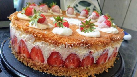 Eine Erdbeer-Käse-Sahnetorte steht auf einem schwarzen Kuchenständer, dekoriert mit frischen Erdbeeren und Sahne.