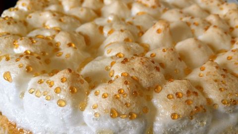 Ein goldbräunlicher Stachelbeerkuchen mit Baiser-Oberfläche, frisch gebacken und auf einem Tisch präsentiert.