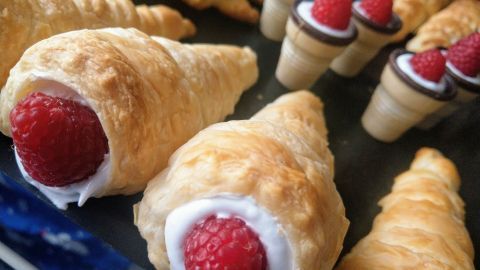 Cremige Schillerlocken mit frischen Himbeeren ragen aus goldbraunem Gebäck, umgeben von ähnlichen süßen Leckereien.