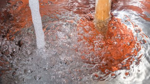 Brauner Kaffeesatz ist im Wasser sichtbar, während er durch einen Abfluss fließt, wobei Blasen aufsteigen und schaumiges Wasser entsteht.
