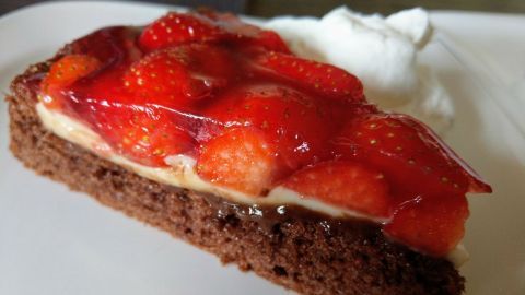 Eine Schoko-Erdbeertorte liegt auf einem Teller, mit frischen Erdbeeren und Sahne daneben. Sie sieht köstlich aus.