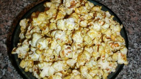 Ein schwarzer Teller voller Popcorn liegt auf einem marmorierten Tisch, umgeben von verschiedenen Gewürzbehältern für Asia Style.