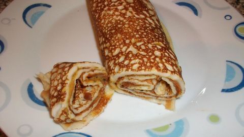 Ein Eierpfannkuchen mit Möhrchenfüllung liegt auf einem Teller, daneben eine Portion in einer kleinen Rolle, appetitlich angerichtet.