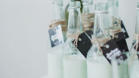 Glasflaschen mit selbstgemachter Mandelmilch stehen auf einem Tisch, dekoriert mit natürlichen Elementen.