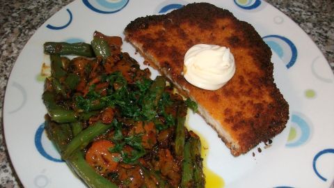 Ein paniertes Schnitzel liegt neben einer Mischung aus Karotten und Bohnen auf einem bunten Teller.