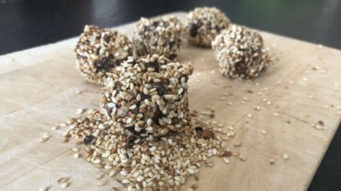 Energiebällchen ohne Zucker liegen auf einem Holzbrett, umgeben von zerstreuten Sesamsamen, bereit zum Genießen.
