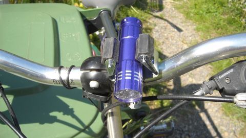 Eine Taschenlampe ist stabil an den Fahrradlenker montiert, während sie auf einem schmalen Weg in der Natur steht.