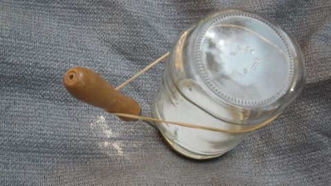 Ein Twist-Off-Glas liegt auf einem grau gemusterten Untergrund, während ein Holzwerkzeug den Deckel mühelos öffnet.