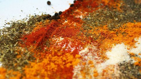 Eine Vielzahl von farbigen Gewürzen liegt verstreut auf einer weißen Fläche, ideal für selbstgemachtes Taco-Gewürz.