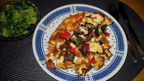 Auf einem Teller liegt ein bunter Gemüse-Schmarren mit Paprika und Zucchini, daneben eine Schüssel mit frischem Salat.