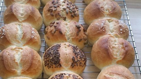 Frisch gebackene Weizenbrötchen liegen auf einem Holzgestell, goldbraun mit verschiedenen Toppings zur Dekoration.