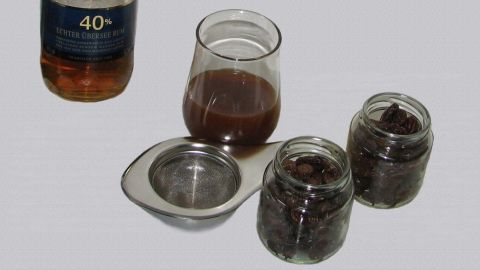 Gläser mit eingelegten Rosinen, eine davon mit Alkohol, stehen auf einem Tisch neben einer offenen Flasche Rum.
