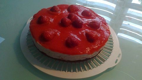 Eine Erdbeertorte steht auf einem weißen Teller und glänzt mit einem frischen Erdbeerspiegel unter hellem Licht.