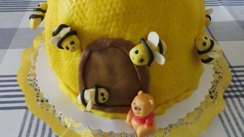 Eine bienenförmige Torte, gelb dekoriert mit kleinen Bienen und einem Eingang, steht auf einem Tisch in einem hellen Raum.