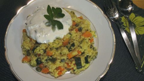 Bunter Karotten-Zucchini-Bulgur liegt auf einem Teller, überzogen mit Zaziki und frischer Kräuter-Dekoration in einer gemütlichen Küche.