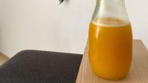 Ein Glas mit erfrischendem Orangensaft steht auf einem Holztisch, umgeben von einem modernen Raum mit Bildern.