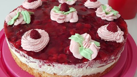 Eine saftige Himbeertorte mit einer Schmand-Sahne-Füllung steht auf einem rosa Teller, dekoriert mit Sahnetupfen und frischen Himbeeren.