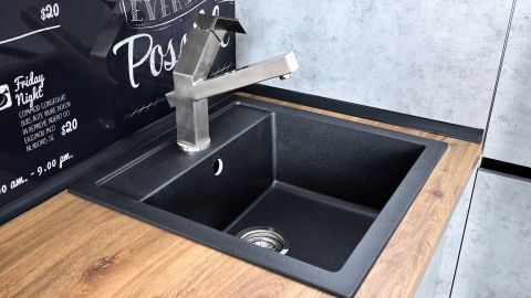 Ein schwarzes Spülbecken steht auf einer Holzarbeitsplatte, bereit zur Reinigung, mit einem modernen Wasserhahn darüber.