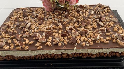 Ein großer, rechteckiger Kinder-Country-Kuchen ohne Backen, bedeckt mit Schokoladenglasur und dekoriert mit Nüssen und Blumen.