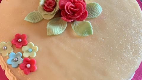 Eine Marzipantorte liegt auf einem rosa Teller, dekoriert mit bunten Zuckerblumen und Blättern, die ansprechend angeordnet sind.