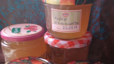 Fünf Gläser mit Apfel-Zitronenmelisse-Gelee stehen hübsch auf einem Tisch, umgeben von einem bunten Hintergrund.
