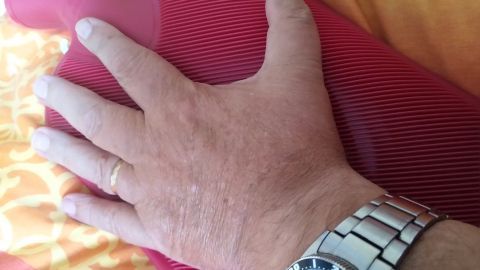 Eine kalte Wärmflasche wird mit einer Hand gehalten, während sie auf einer weichen, bunten Bettdecke liegt, um beim Einschlafen zu helfen.
