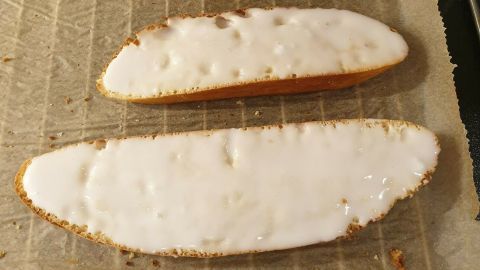 Hefegebäck, das frisch gebacken auf einem Blech mit Backpapier liegt, zeigt verschiedene Größen und einen glasierten Belag.