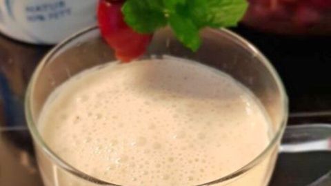 Ein Glas Kirsch-Ayran steht auf einem Tisch, garniert mit Kirschen und Minze, im Hintergrund sind frische Kirschen sichtbar.