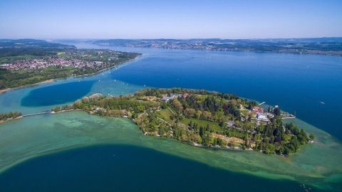 Ein klarer Blick auf die Insel im Bodensee, umgeben von smaragdgrünem Wasser, unter strahlend blauem Himmel.