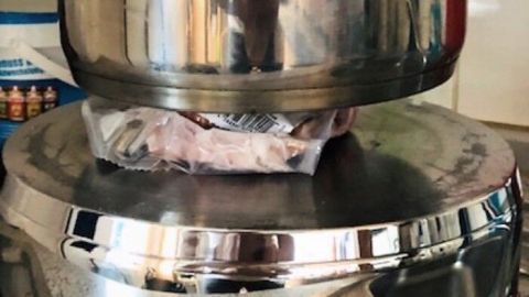 Ein Edelstahltopf steht auf einem anderen Topf und taut Fleisch schnell und schonend, ohne Wärme, im Küchenumfeld auf.